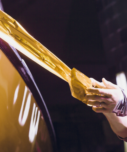 A woman is waxing the hood of a yellow car